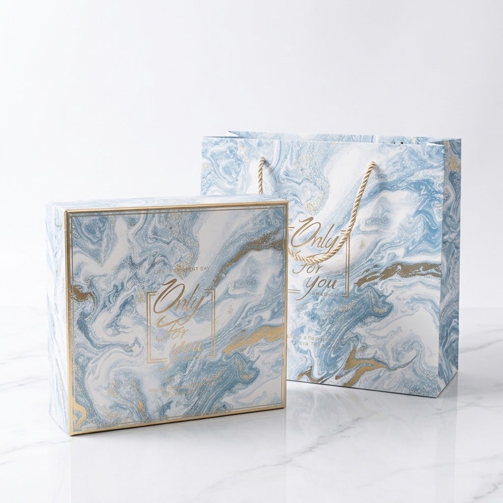 A matching gift box and gift bag set with a blue, white, and gold marble pattern, featuring the text &