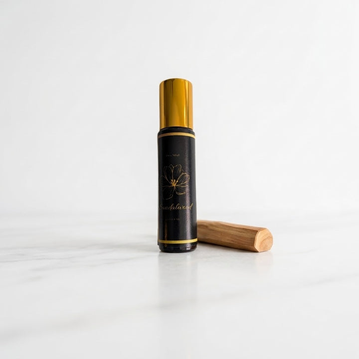A black cylindrical bottle with a shiny gold cap stands on a white marble surface against a white background, with a small wooden stick placed beside it.