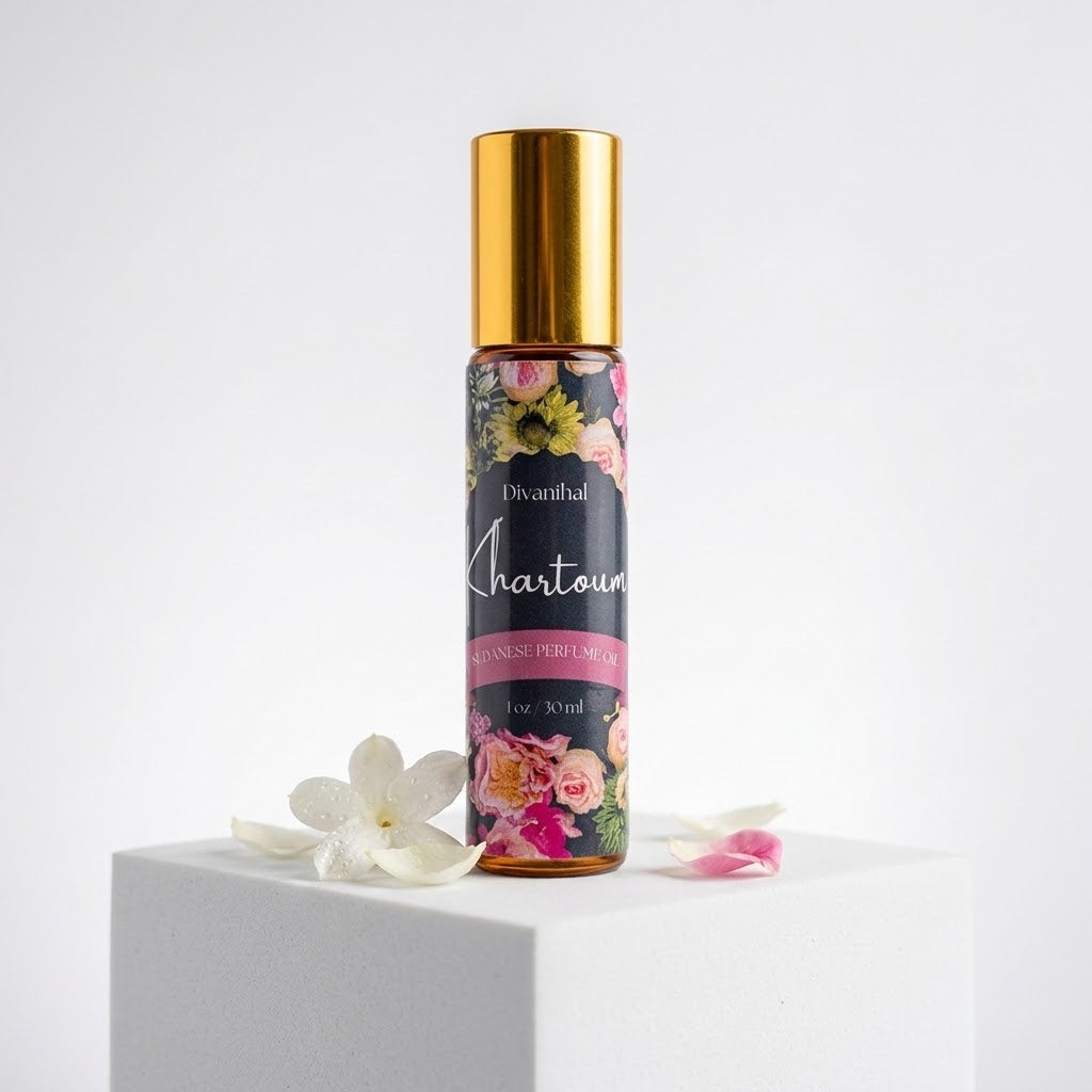 A 10ml roll-on perfume bottle with a shiny gold cap and a floral label, standing on a white pedestal with white flower petals around it against a white background.
