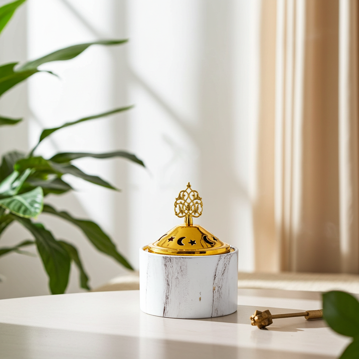 Decorative container with gold lid on a marble surface, plant in the background