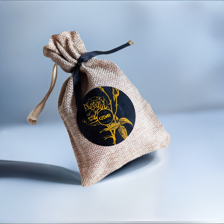 A small burlap sack with a black label featuring a gold floral design, tied with a black ribbon.