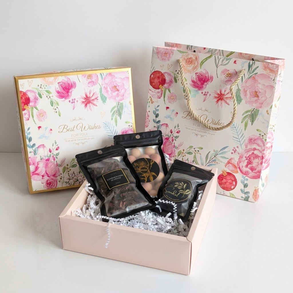 A gift set featuring a pink floral gift box with three black pouches of bakhoor, incense cons and cedar balls inside, alongside a matching pink floral gift bag and a square floral gift box on a white background.