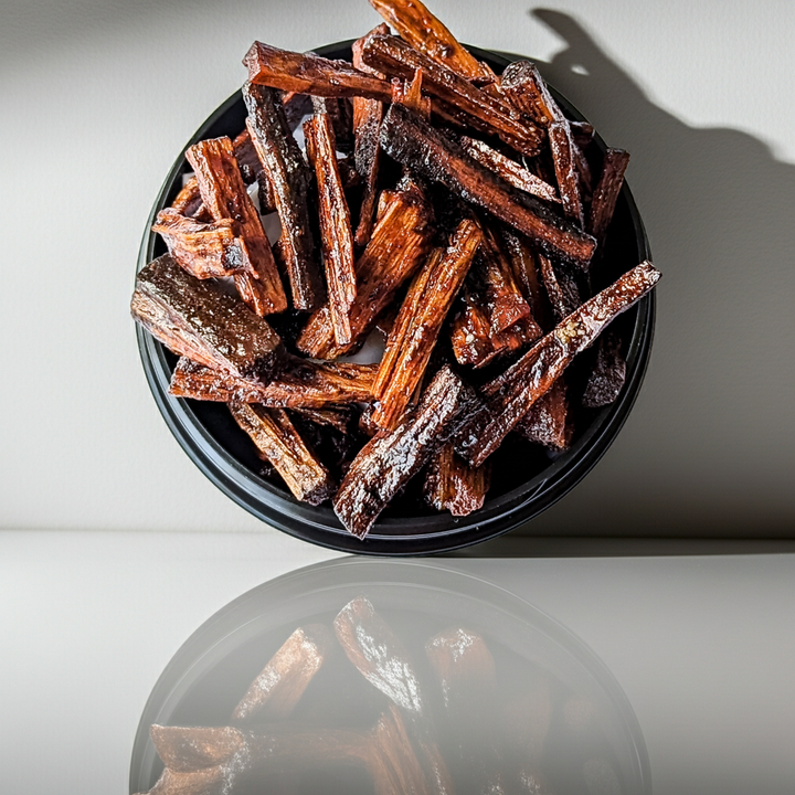 Dried bakhoor sticks in a black bowl on a reflective surface