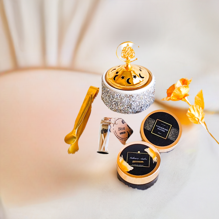 A collection of items including two small containers of Bakhoor, sandalwood and amber scented, with golden decorative elements, a set of mini Mubkhar match sticks, and a mini golden tong, all displayed on a light-colored surface.
