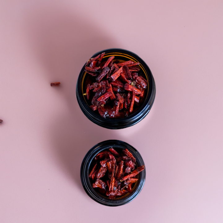 A jar of Sudanese Sandalwood Bakhoor incense with a black lid, placed on a white surface, with decorative elements in the background.