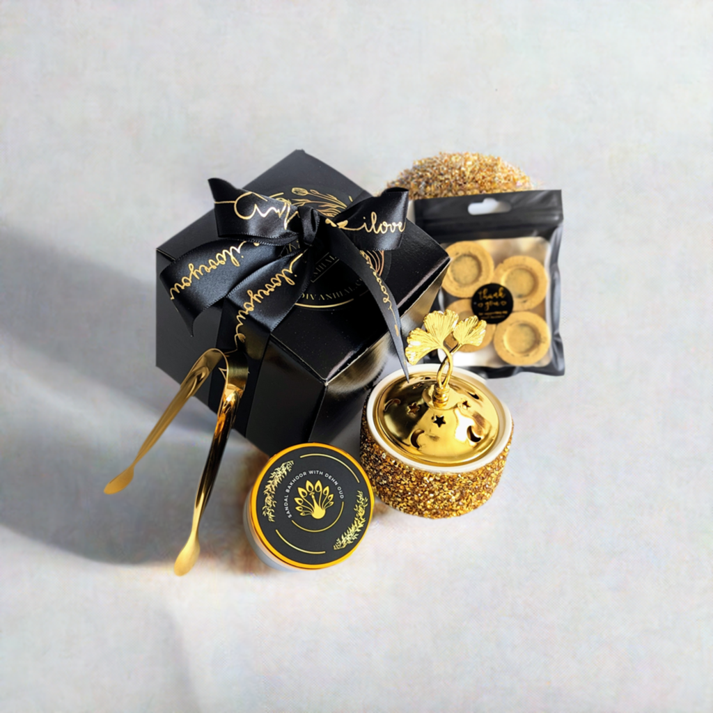 A ready-to-use Bakhoor kit with a black and gold color scheme, including a box of incense, a sandalwood bowl, and gold-colored tongs.
