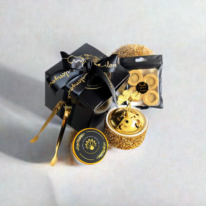 A ready-to-use Bakhoor kit with a black and gold color scheme, including a box of incense, a sandalwood bowl, and gold-colored tongs.