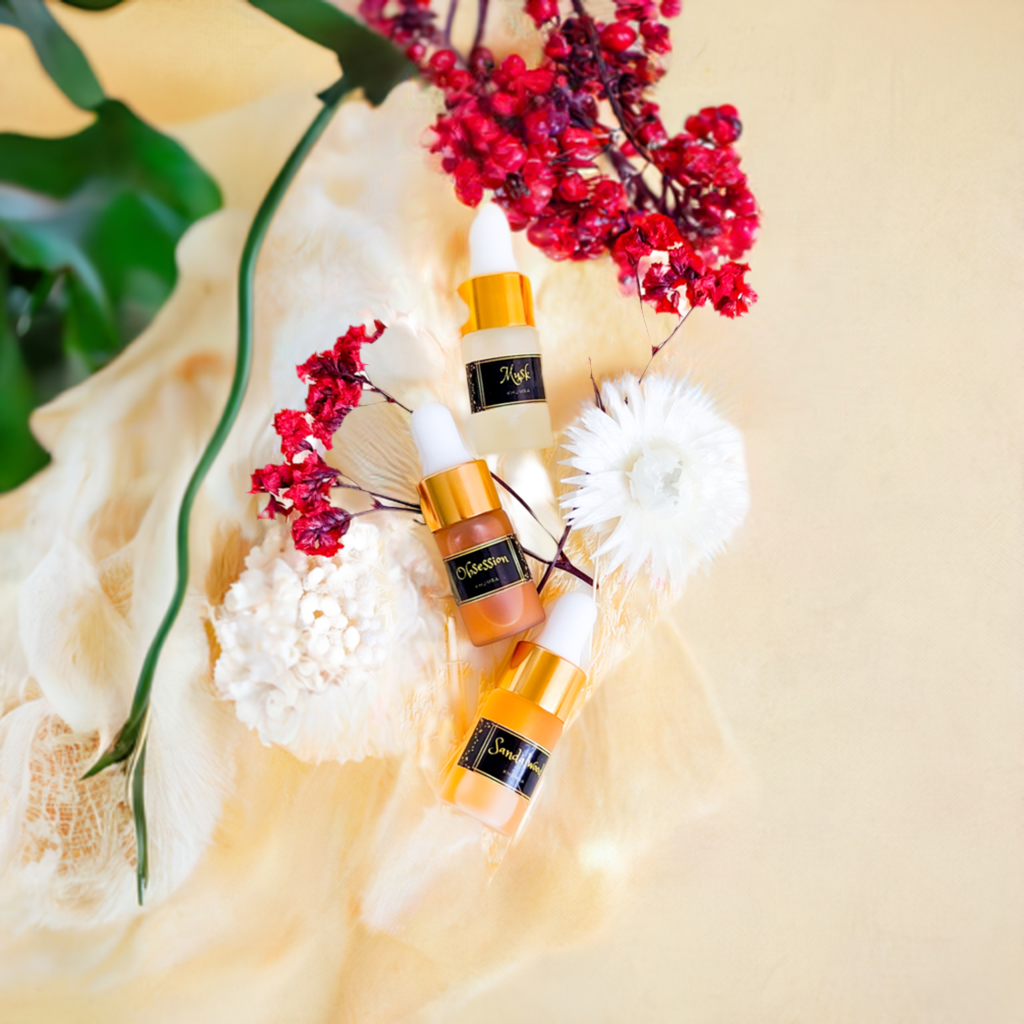 Three small perfume bottles with golden caps, arranged on a pale background surrounded by white flowers and red berries.