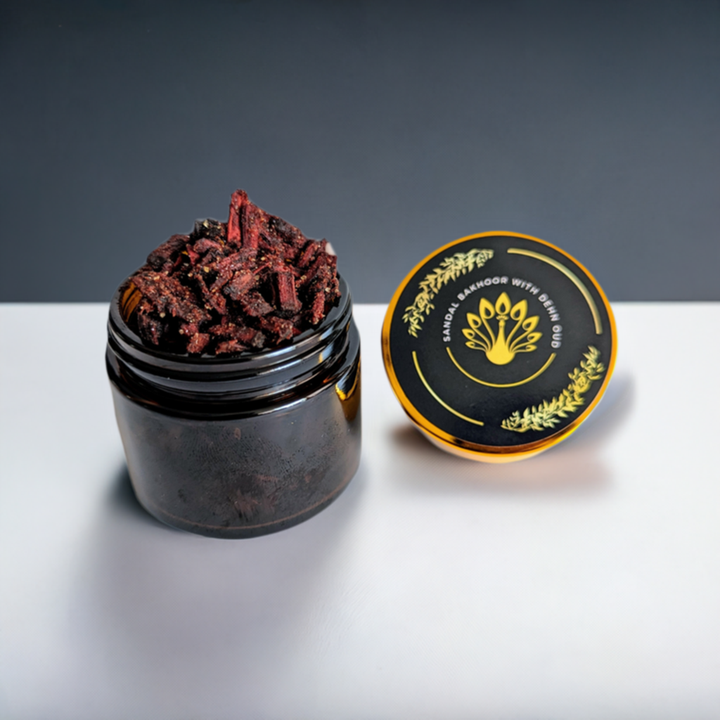 A jar of Sudanese Sandalwood Bakhoor incense with a black lid, placed on a white surface, with decorative elements in the background.