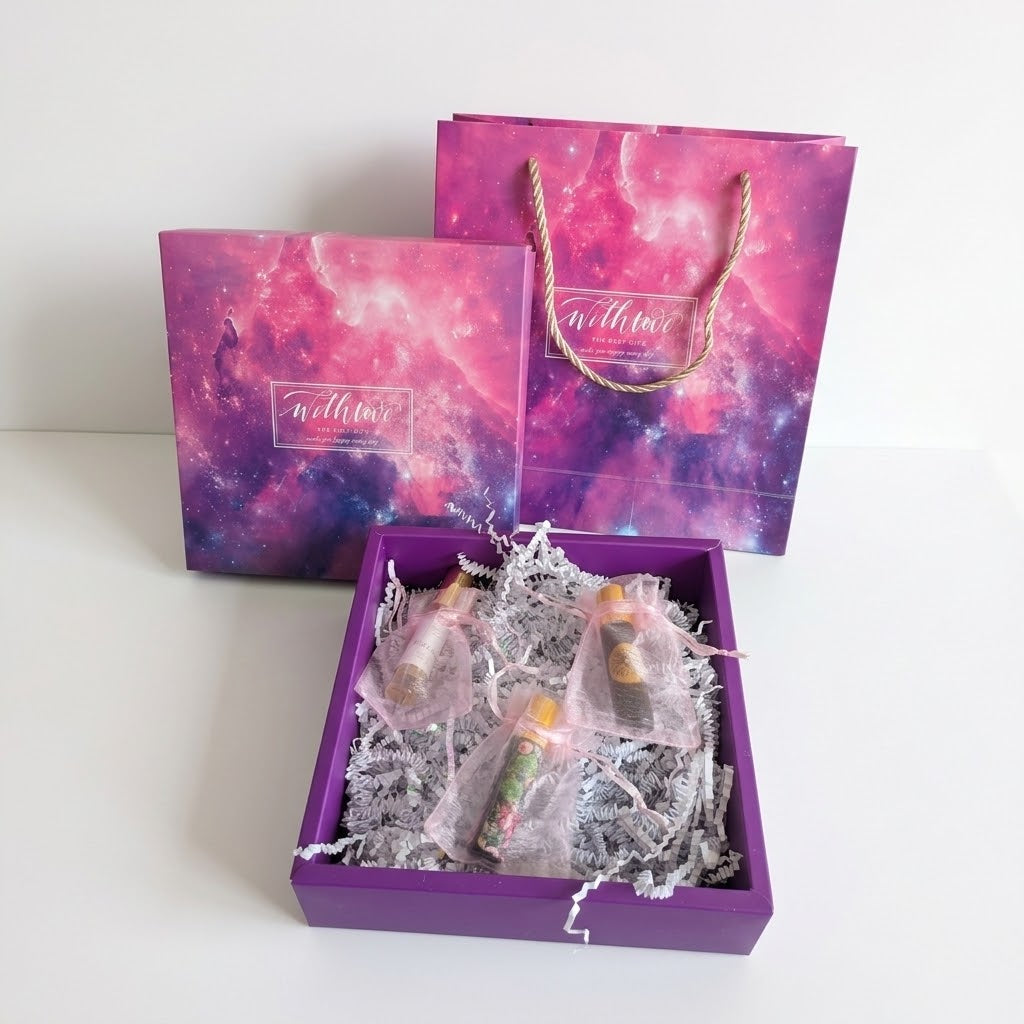 A purple gift box filled with small individually wrapped items on white crinkle paper, with matching purple and pink galaxy-patterned gift bags behind it on a white background.